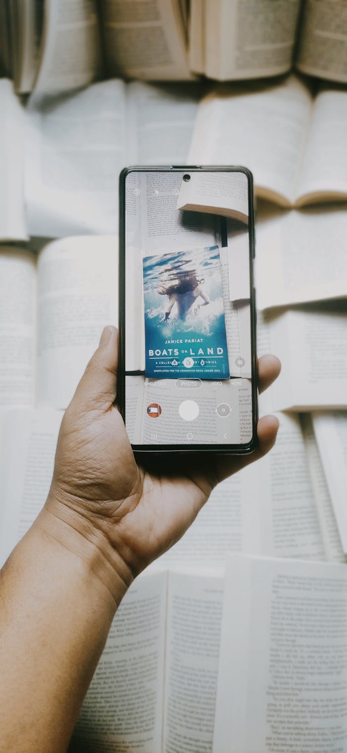 Hand holding a smartphone over open books, capturing an engaging photo.
